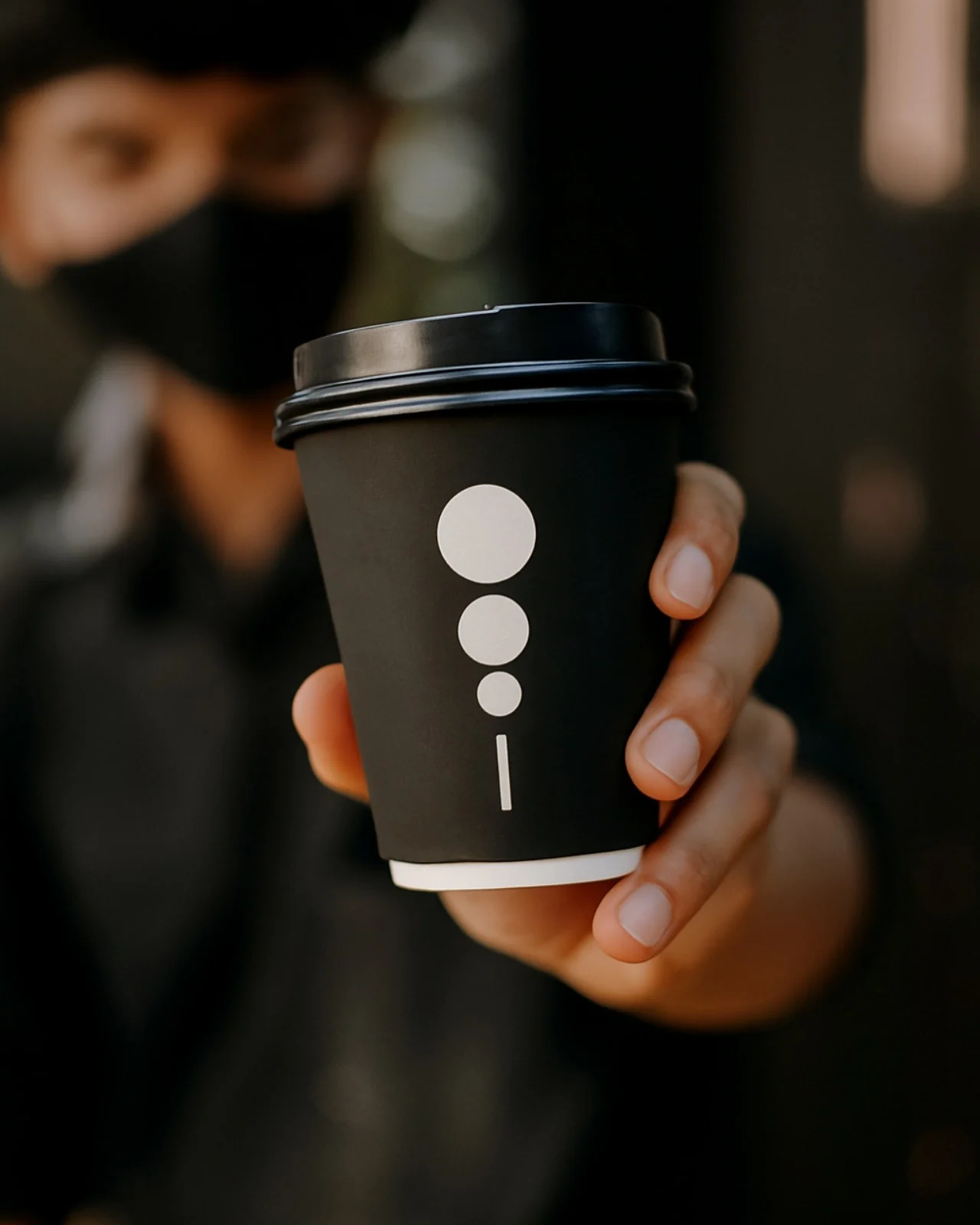 A person presenting a black KAFI takeaway cup